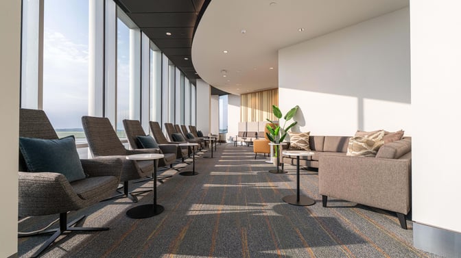 The Club GRR lounge at Grand Rapids Airport features comfortable seating with individual tables and large windows offering runway views.