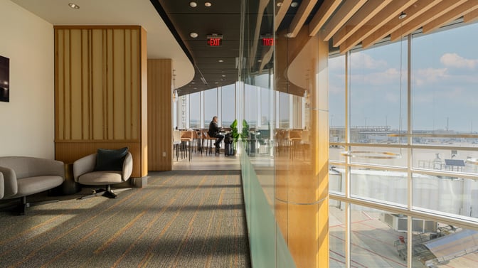 The seating area in The Club GRR at Grand Rapids Airport offers comfortable chairs and tables with expansive tarmac views.