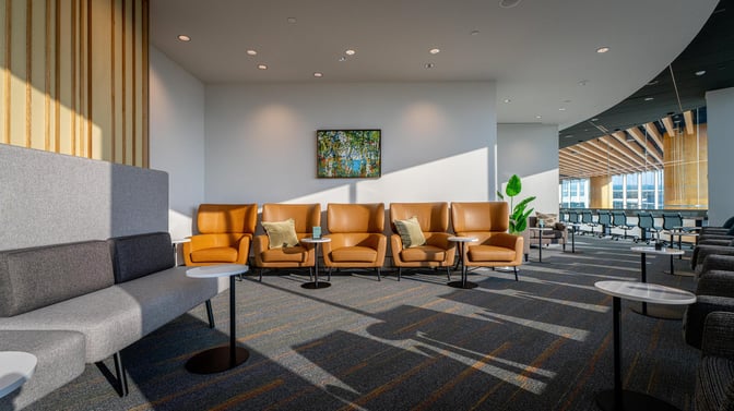 The seating area in The Club GRR features comfortable chairs and tables, offering a relaxing space with airport views.