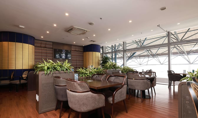 The seating area in SH Premium Lounge at Noi Bai International Airport features tables and chairs with airport views through large windows.