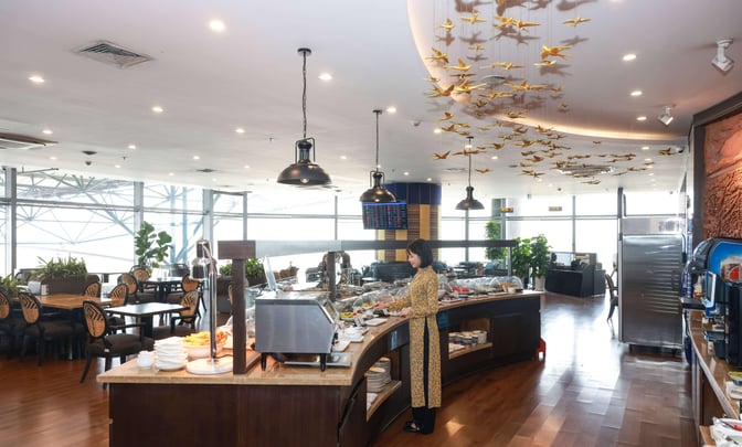 The SH Premium Lounge in Hanoi features a self-serve buffet area with various food options and seating overlooking the airport.