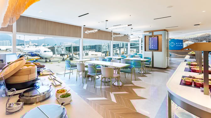 The Kyra Lounge at Hong Kong International Airport features a dining area with tables, chairs, and a self-serve food station.