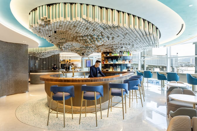 The bar area at Kyra Lounge in Hong Kong International Airport features a circular counter with seating and a variety of spirits.