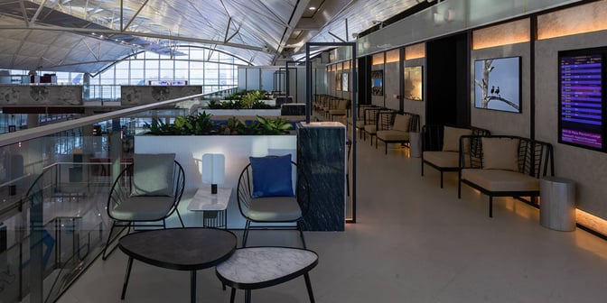 The Plaza Premium Lounge near Gate 60 at Hong Kong International Airport features seating areas with tables and airport views.