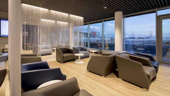 The seating area in Hugo Junkers Lounge at Dusseldorf Airport features comfortable chairs and tables with views of the tarmac.