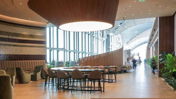 The IGA Lounge at Istanbul Airport features a spacious seating area with tables and chairs, adjacent to large windows.