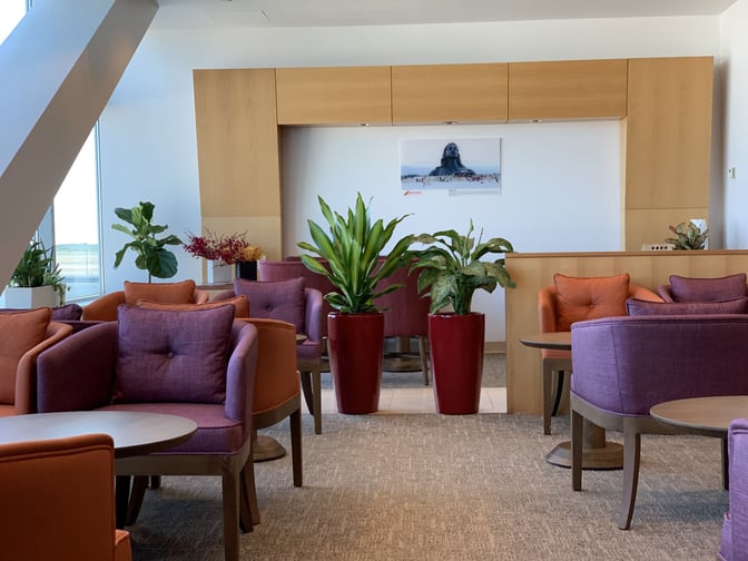 Seating area in the Air India Maharajah Lounge at JFK Airport features comfortable chairs and tables with decorative plants.