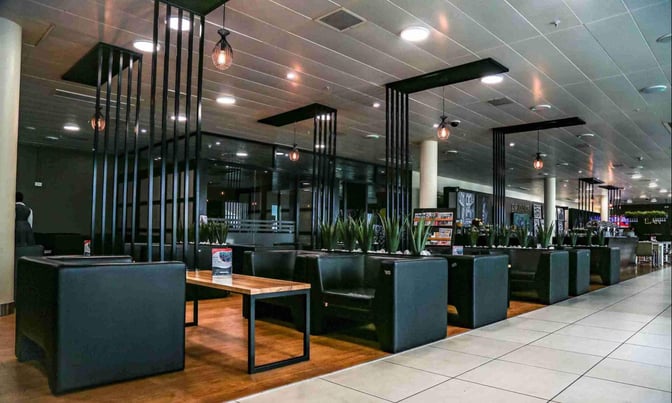 The CIP Lounge at Julius Nyerere International Airport features booth seating with tables and decorative plants, providing a comfortable waiting area.