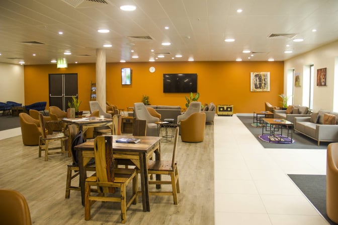 The Twiga Lounge at Julius Nyerere International Airport features a seating area with tables, chairs, and a large wall-mounted television.