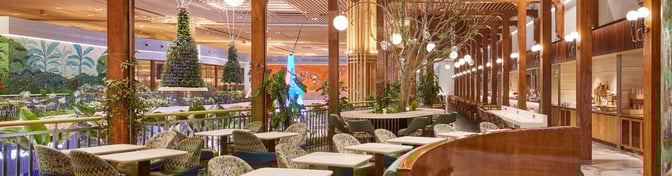 The seating area in the 080 Domestic Lounge at Kempegowda Airport features tables and chairs with surrounding greenery and decorative elements.