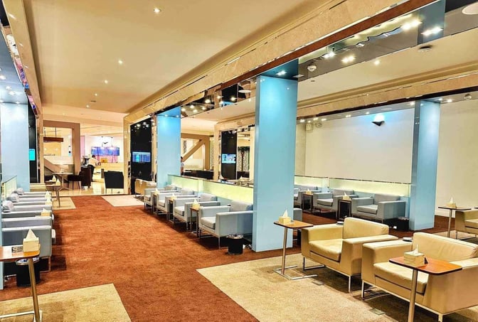 The Wellcome Lounge at King Fahd International Airport features comfortable seating with individual tables, providing a relaxing space for travelers.