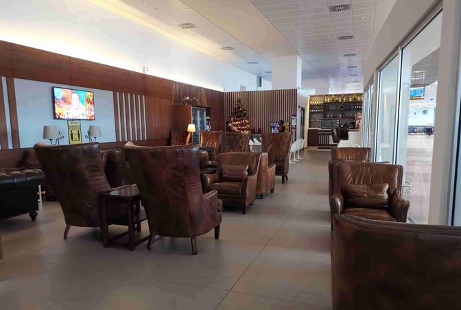 The Sanbra Priority Lounge at Kotoka International Airport features comfortable seating with a view of the tarmac and a bar area.