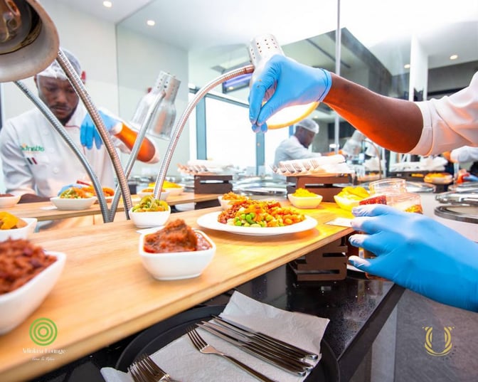 A chef at U Lounge in Kotoka International Airport prepares and presents a variety of plated dishes at a serving station.