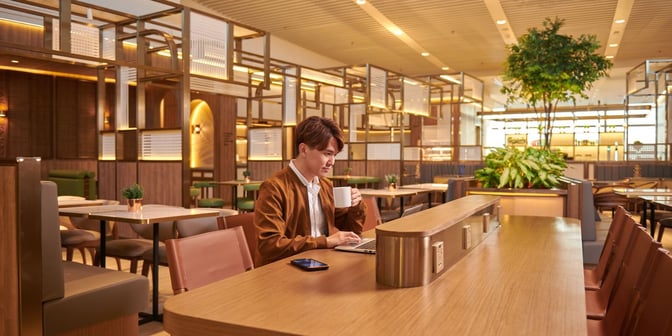 The Plaza Premium Lounge at Kuala Lumpur International Airport features a seating area with tables, chairs, and accessible power outlets for travelers.