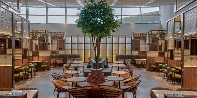 The seating area in Plaza Premium Lounge at Kuala Lumpur International Airport features tables, chairs, and booth seating with a central tree.