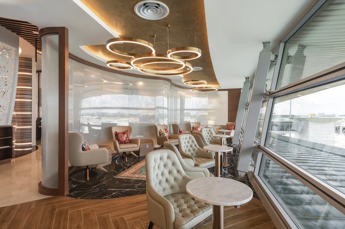 The seating area in the Travel Club Lounge at Kuala Lumpur International Airport features comfortable chairs and tables with airport views.