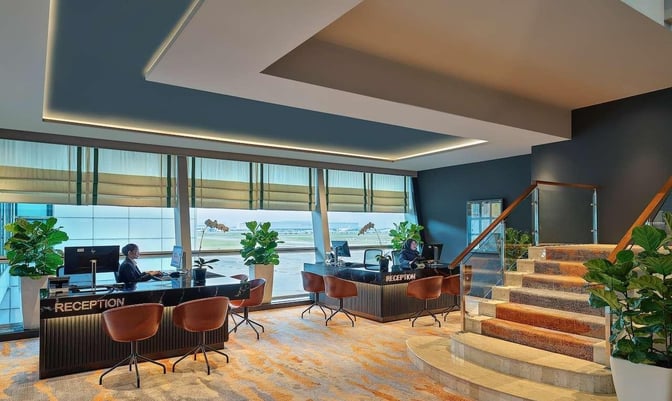The reception area of the Sky Suite Airport Lounge at Kuala Lumpur International Airport features desks with seating and large windows.