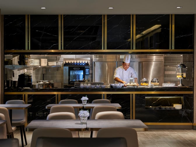 The dining area at Plaza Premium Lounge, Langkawi Airport, features a chef preparing food behind a counter with seating available.