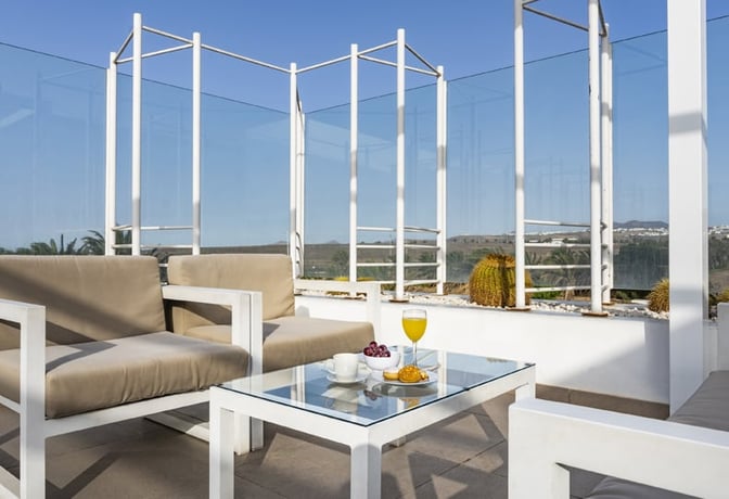 Outdoor seating at Sala VIP Guacimeta features cushioned chairs and a glass table with refreshments, offering views of the surrounding landscape.