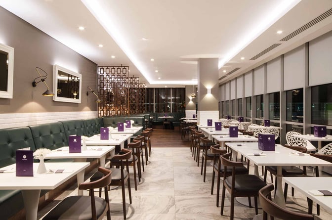 The dining area at No1 Lounge, London Gatwick Airport, features table seating with menus and overlooks the airport through large windows.