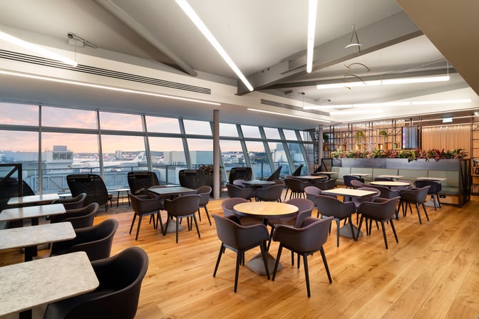 The Club Aspire Lounge at London Gatwick Airport features a seating area with tables and chairs, offering views of the runway.