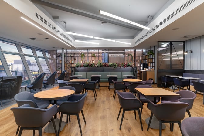 The seating area in Club Aspire Lounge at London Gatwick Airport features tables and chairs with views of the airport tarmac.