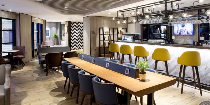 The Plaza Premium Lounge at London Heathrow features a bar with counter seating and a communal table equipped with charging ports.