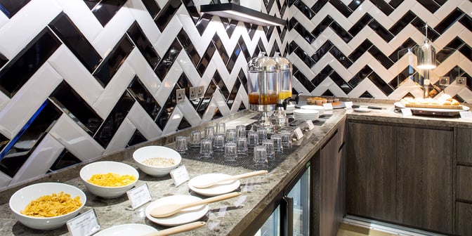 Self-serve breakfast station at Plaza Premium Lounge, London Heathrow, offers cereals, pastries, and juice with labeled selections.