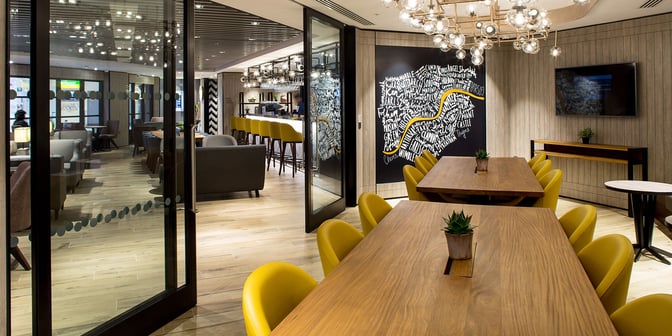 The Plaza Premium Lounge at London Heathrow Airport features a bar area with high stools and a communal table for dining.