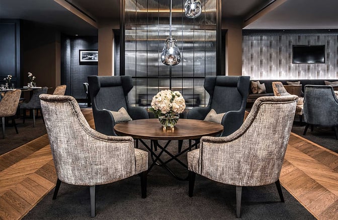 The seating area at No1 Lounge, London Luton Airport, features comfortable chairs around a central table with decorative flowers.