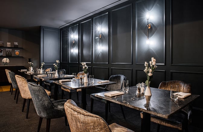 The dining area at No1 Lounge, London Luton Airport, features tables set with glassware and flowers, offering a comfortable seating arrangement.