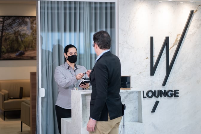 The entrance to W Lounge Londrina features a reception desk where a staff member assists a guest with check-in.