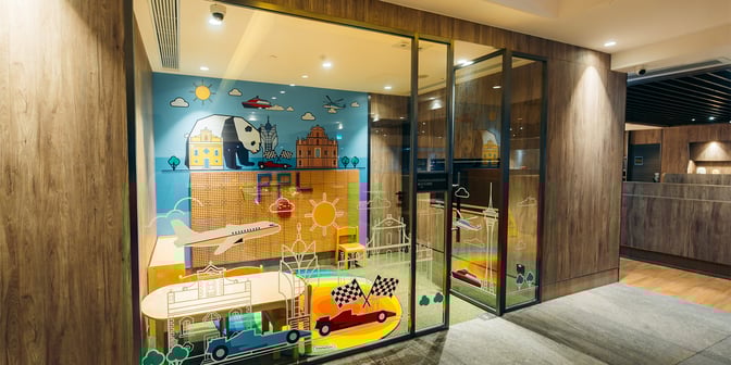 The children's play area at Plaza Premium Lounge, Macau International Airport, features colorful wall art and small tables with chairs.