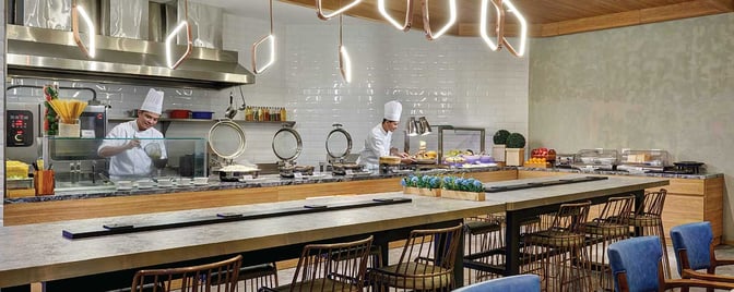 The dining area at Plaza Premium Lounge, Mactan-Cebu International Airport, features a live cooking station with chefs preparing meals.