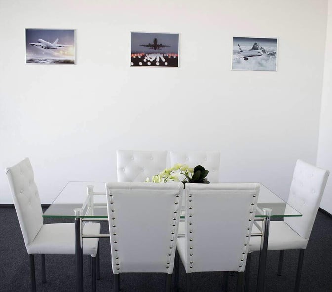 A seating area in Manas International Airport's business lounge features a glass table with cushioned chairs and aviation-themed wall art.