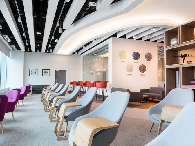 The seating area in Manchester Airport's Escape Lounge features comfortable chairs and sofas with wall clocks displaying various time zones.