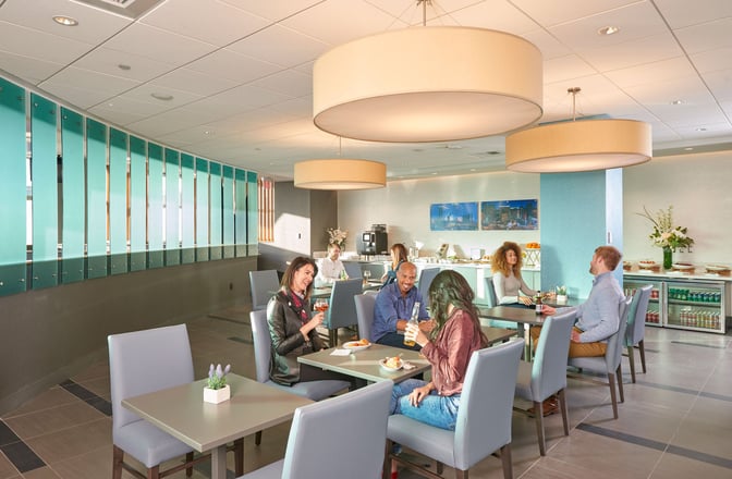The Club LAS lounge at McCarran International Airport features a seating area with tables, chairs, and a self-serve refreshment station.
