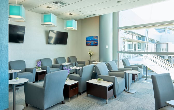 The seating area in The Club LAS at McCarran International Airport features armchairs, small tables, and views of the airport exterior.