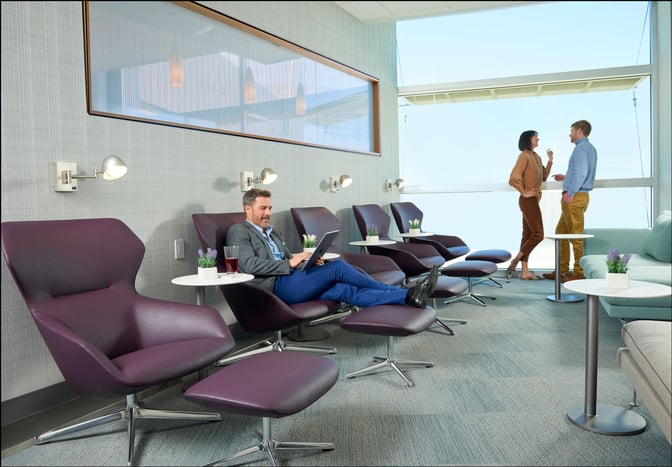 The seating area in The Club LAS at McCarran International Airport features lounge chairs with footrests and small side tables.