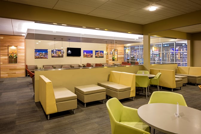 The Club LAS lounge at McCarran International Airport features varied seating options with tables, couches, and a view of the duty-free area.