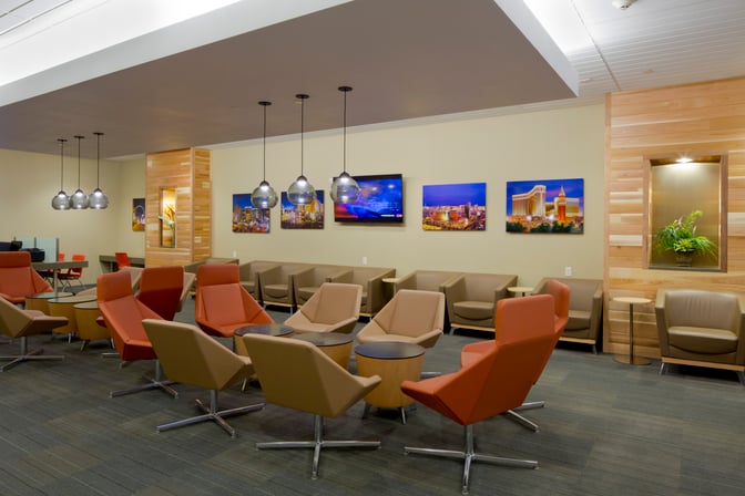 The seating area at The Club LAS features comfortable chairs and tables, with wall-mounted artwork and overhead lighting.