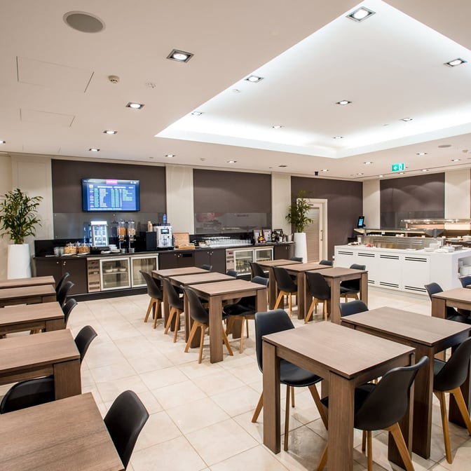 The Marhaba Lounge at Melbourne Airport features a dining area with tables and chairs, alongside a self-serve beverage station.