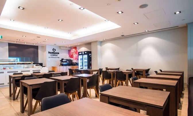 The seating area in the Marhaba Lounge at Melbourne Airport features tables and chairs near a self-service coffee station.