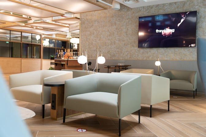 The HelloSky lounge at Milan Bergamo Airport features comfortable seating with nearby charging outlets and a visible bar area in the background.