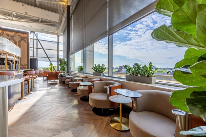 The Aspire Lounge at Montreal-Trudeau International Airport features seating with tables and views of the airport runway through large windows.