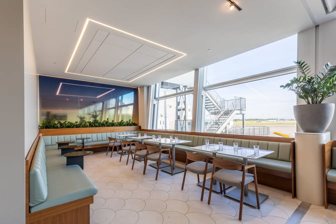 Booth and table seating in the Aspire International Lounge at Montreal-Trudeau Airport offers views of the tarmac through large windows.