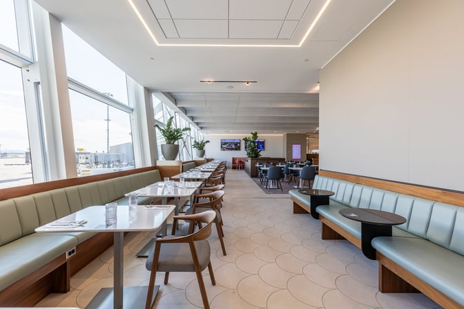 The Aspire International Lounge at Montreal-Trudeau Airport features booth and table seating with views of the tarmac through large windows.