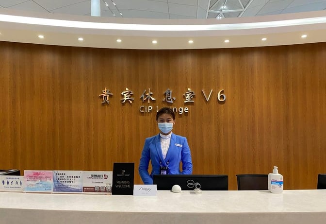 The reception desk at the V6 Business Lounge in Nanjing Lukou International Airport features a staff member ready to assist guests.