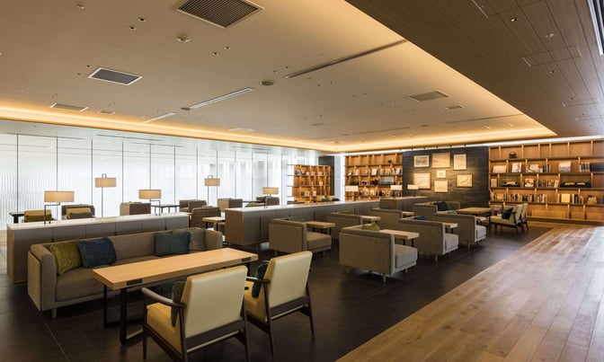 The lounge at New Chitose Airport features comfortable seating with tables and bookshelves, providing a relaxing space for travelers.