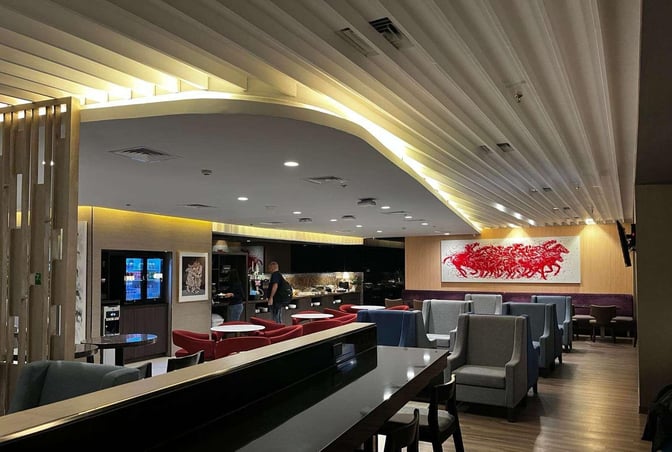 The lounge at Ninoy Aquino International Airport features a seating area with tables and chairs, and a self-serve food station.
